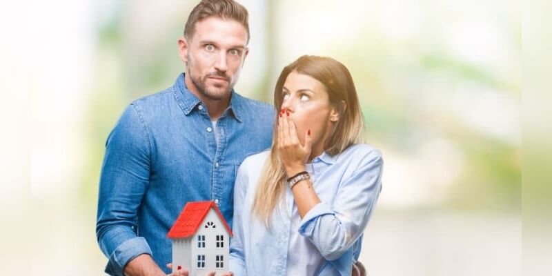 Image of a man and woman looking scared with a house after bidding at an auction. You can't pull out!
