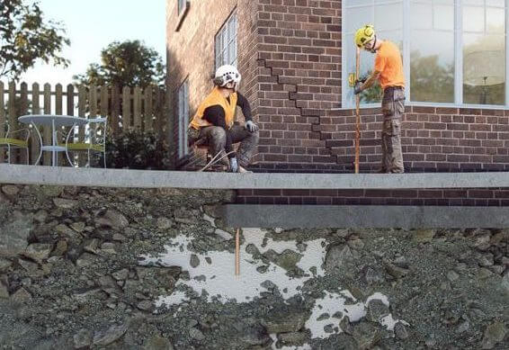 An image of two builders injecting resin into void beneath a house suffering from subsidence. 