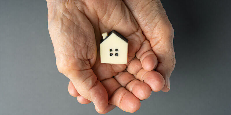 Will inheriting a property affect my benefits? Elderly woman hands holds a little toy house. 