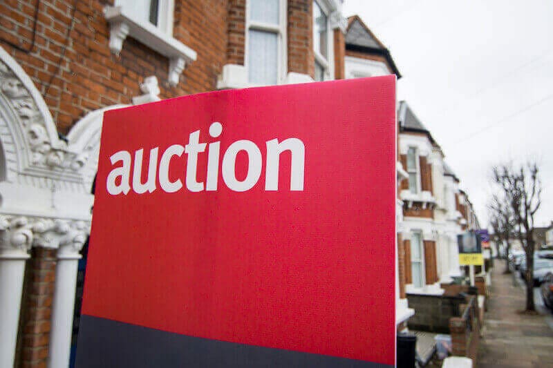 A picture of an auction for sale board outside a house.