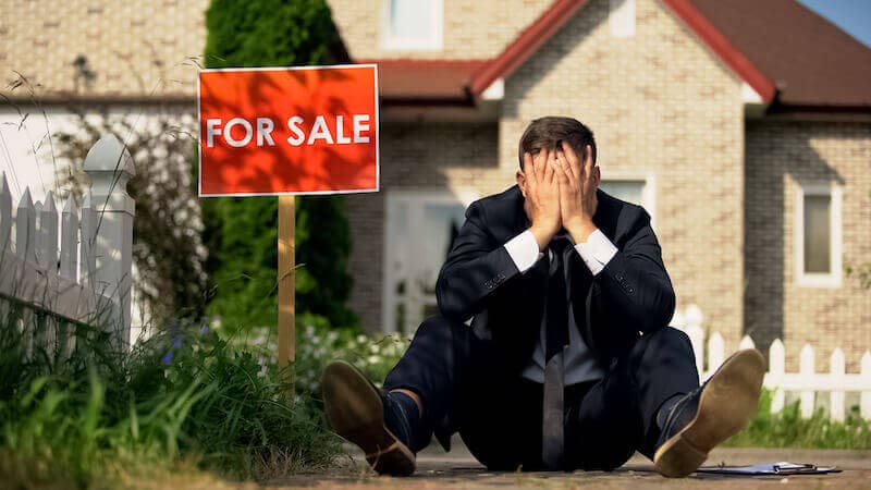A man sat outside a house for sale that has just fallen through.