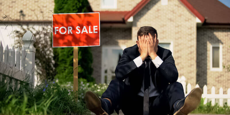 A man sat outside house for sale looking frustrated and upset.