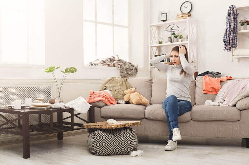 An image of a lady sat in a messy living room.
