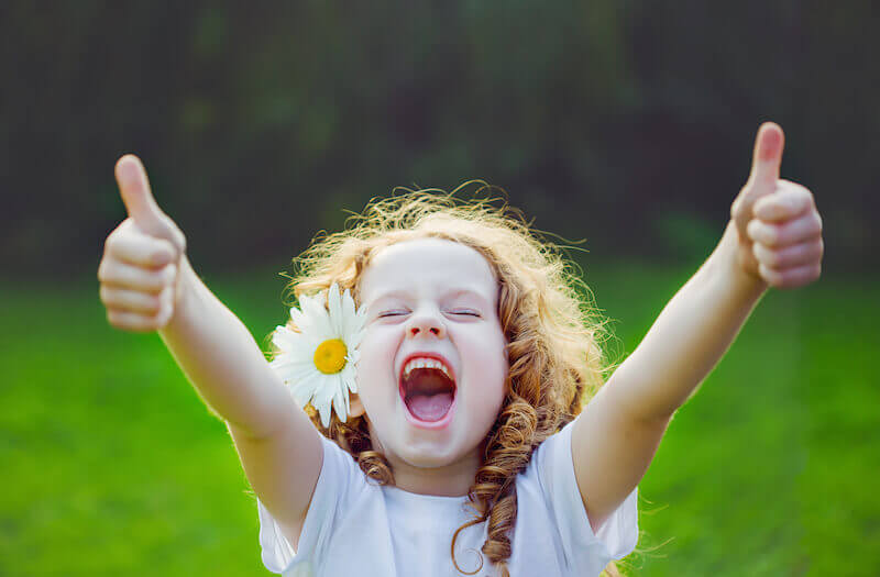 A smiling child with a flower in her hair showing thumbs up.